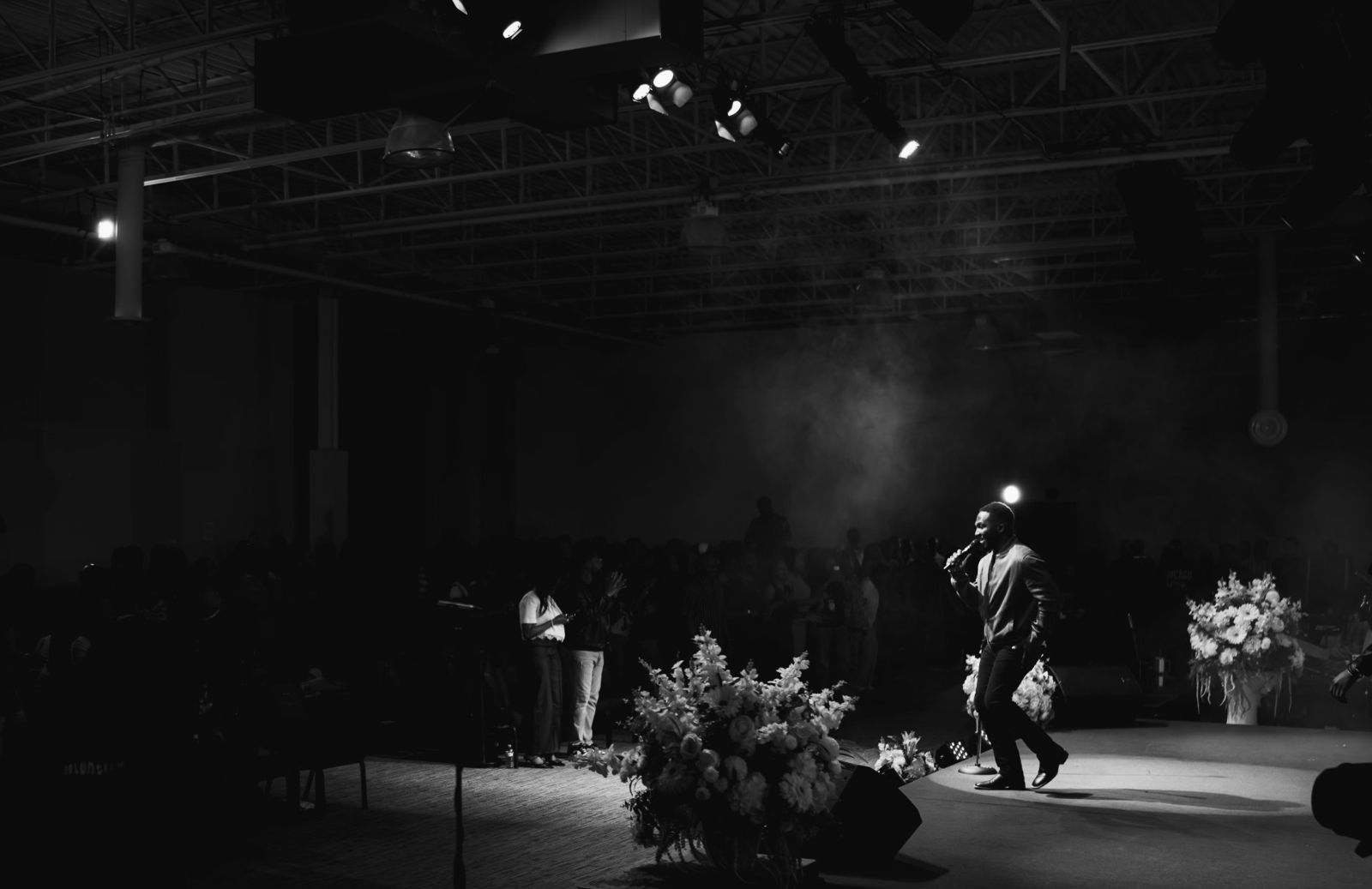 Divine performing under a single spotlight in a large hall, black and white